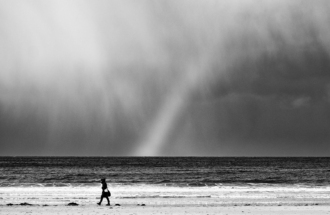 Femme qui marche le long du bord de mer sous un arc en ciel