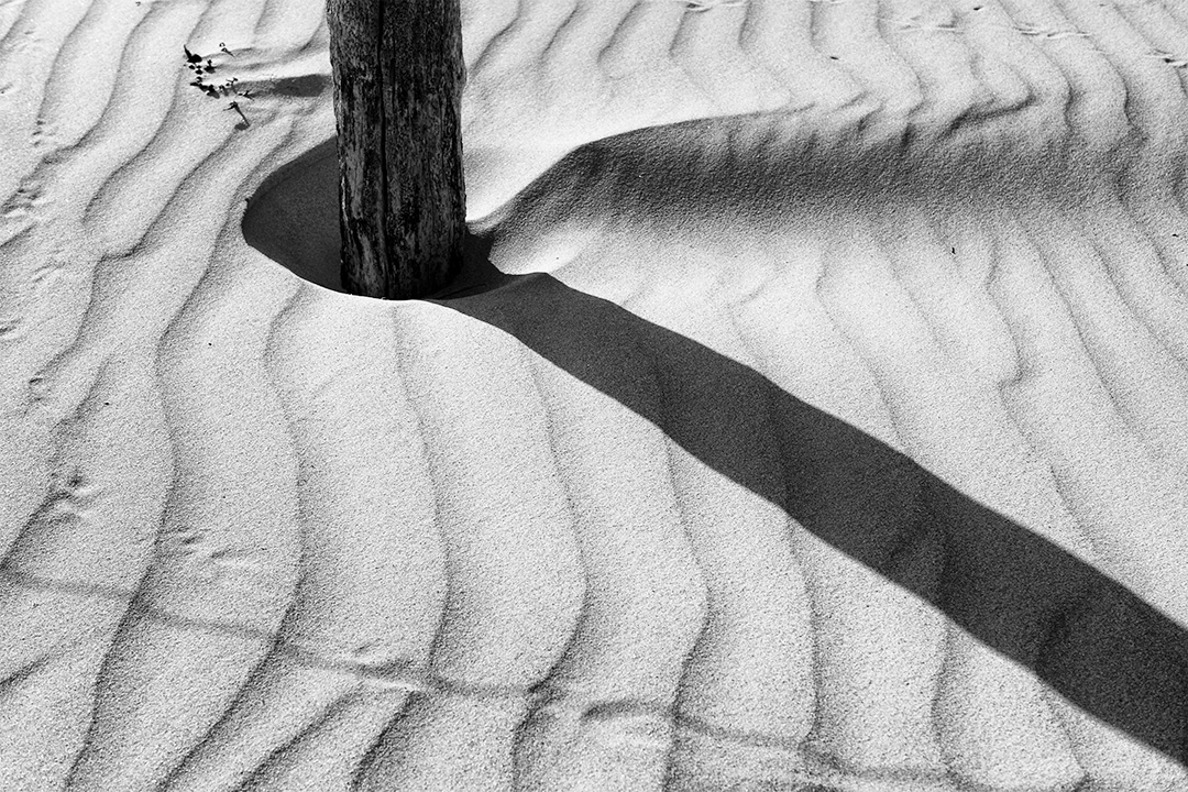 Ombre d'un plot de clôture sur le sable d'une dune
