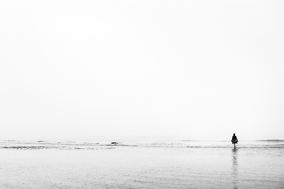 Femme se promenant les pieds dans l'eau de mer sous une brume maritime