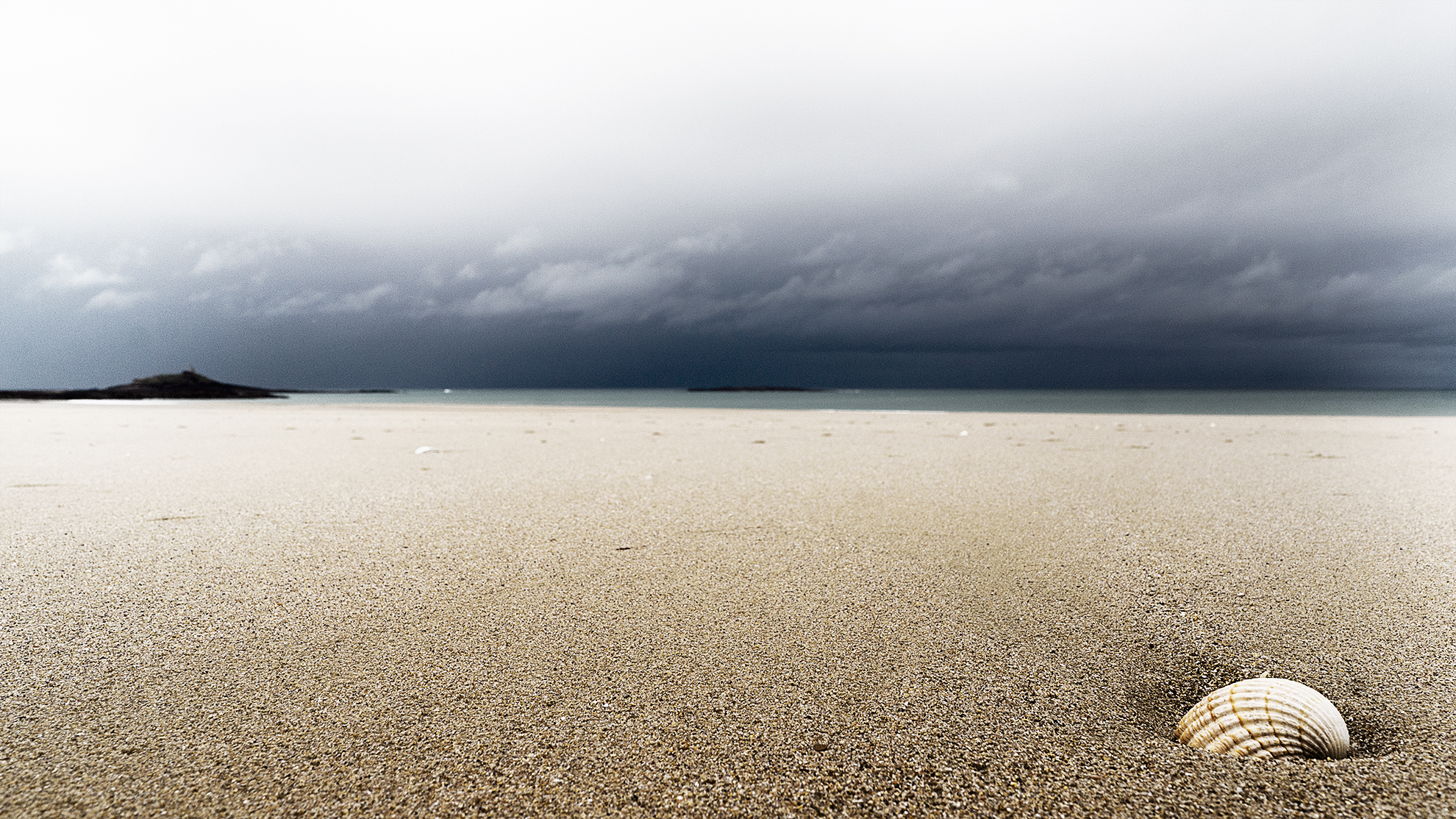 Coquille de bucarde posée sur le sable face à la mer et à l'Îlot St-Michel de Sables d'Or les Pins